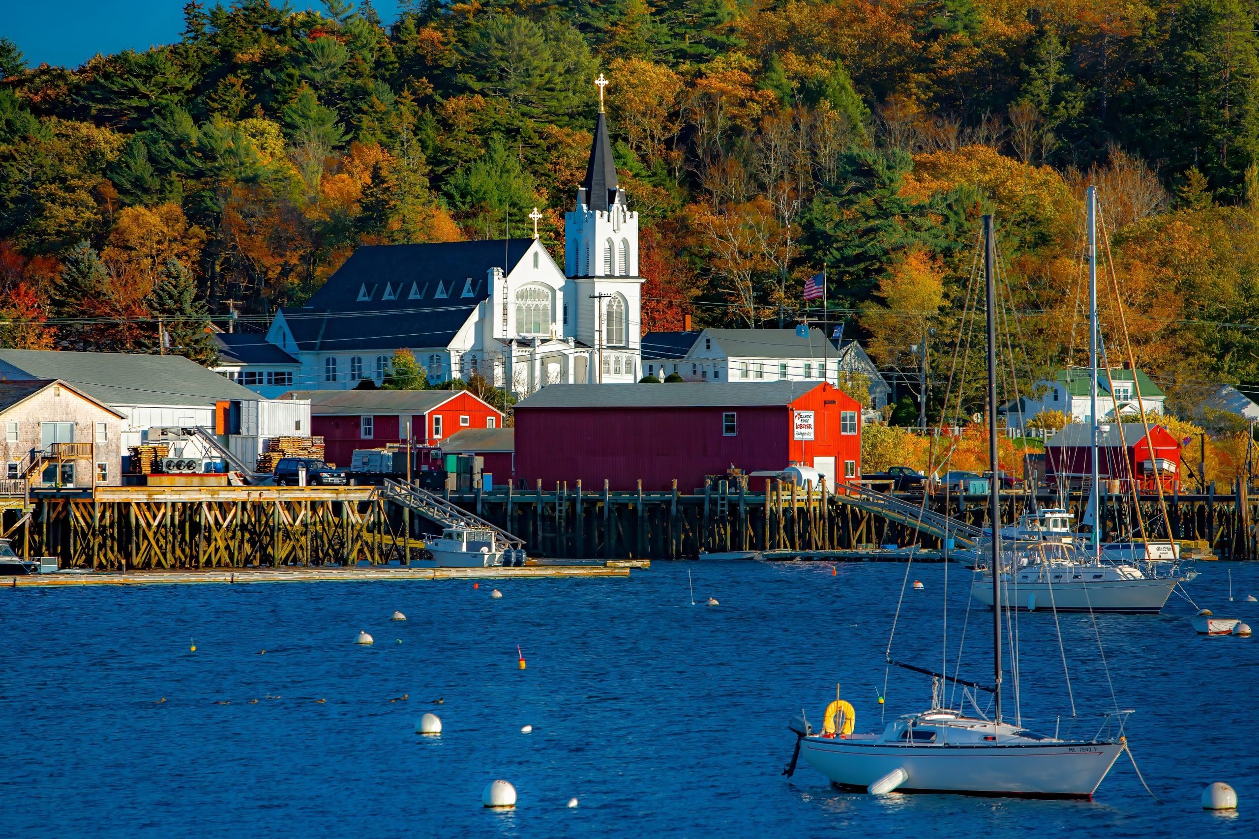Boothbay Harbor in Maine met witte kerk, rode loodsen en zeilboten in de haven